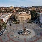 Vedere aeriană a orașului Kutaisi, cu piața centrală și fântâna Colchis, înconjurată de clădiri istorice. În fundal, Catedrala Bagrati domină orașul.