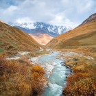 Râul Enguri, cu apele sale lăptoase, traversează o vale aurie în Svaneti. Curge prin liniște și pante line, cu vârfurile Caucazului pe fundal.