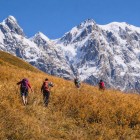 Drumeție prin ierburi aurii la poalele ghețarului Shkhara din Svaneti. Traseul urcă prin liniște și panorame deschise, iar vârfurile înzăpezite însoțesc fiecare pa