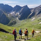 Drumeți pe un traseu din Marele Caucaz, între văi verzi și creste stâncoase. Poteca coboară prin liniște deschisă, iar zăpada rămasă însoțește fiecare pas.