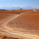 Drum de pământ în deșertul Agafay, printre dealuri aride și spații deschise, cu Munții Atlas în fundal.