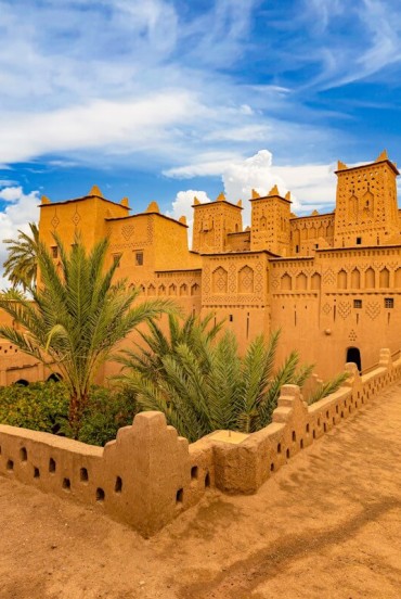 Vedere asupra unei kasbah tradiționale din Ouarzazate, între ziduri ocru, curți interioare, palmieri și detalii ale arhitecturii berbere marocane.