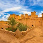 Vedere asupra unei kasbah tradiționale din Ouarzazate, între ziduri ocru, curți interioare, palmieri și detalii ale arhitecturii berbere marocane.