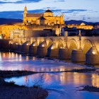 Podul Roman conduce spre impresionanta Moschee-Catedrală din Córdoba, unde luminile, istoria și farmecul andaluz se reflectă în râul Guadalquivir într-un decor memorabil.