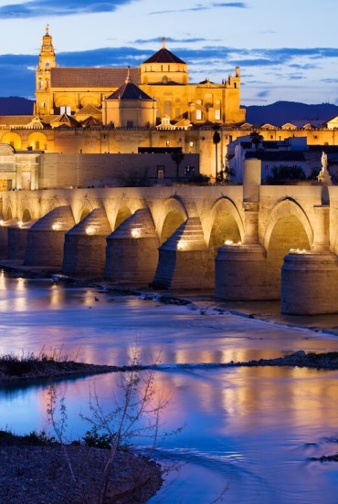 Podul Roman conduce spre impresionanta Moschee-Catedrală din Córdoba, unde luminile, istoria și farmecul andaluz se reflectă în râul Guadalquivir într-un decor memorabil.