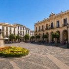 Plaza de España este inima orașului Ronda, înconjurată de clădiri istorice elegante, arcade și grădini îngrijite, cu statuia lui Blas Infante în centru.