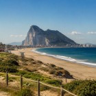 Plaja întinsă din Gibraltar conduce privirea spre impunătoarea Stâncă, acolo unde Marea Mediterană întâlnește Oceanul Atlantic într-un peisaj spectaculos și memorabil.