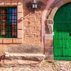 Detaliu al unei case tradiționale din piatră din Castrillo de los Polvazares, cu poarta verde caracteristică și arhitectura ce amintește de trecutul cărăușilor.