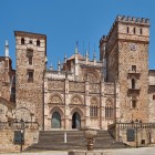 Fațada gotico-mudejară a Mănăstirii Regale Santa María de Guadalupe domină piața satului, cu turnuri crenelate și rafinate detalii sculptate, în Extremadura.