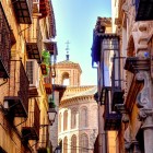 Calle de San Bartolomé dezvăluie Toledo autentic, cu balcoane din fier, case istorice și absida mudéjar a bisericii, lângă Palatul Pantoja y Angulo.