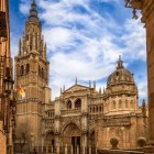 În inima orașului Toledo, fațada gotică a Catedralei Primatiale se înalță printre clădiri istorice, remarcată prin portaluri sculptate, pinacluri și turnul din secolul al XV-lea.
