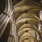 Privirea urcă de-a lungul pilonilor gotici ai Catedralei din Toledo spre bolțile în ogivă, luminate de vitralii care accentuează verticalitatea navei.