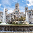 Fuente de Cibeles domină piața cu carul zeiței tras de lei; în fundal, turnurile neogotice ale Palacio de Cibeles evocă Madridul monumental.