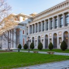 Fațada laterală a Muzeului Prado desfășoară arcade și pilaștri neoclasici de-a lungul grădinii; ritmul regulat al pietrei dezvăluie proiectul iluminist al lui Villanueva.