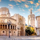 Cu vedere spre Plaza de la Almoina, Catedrala din Valencia dezvăluie romanica Puerta del Palau și turnul El Miguelete; dedicată Adormirii Maicii Domnului de Iacob I, este bazilică minoră din 1886.
