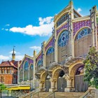 Arhitectura și culoarea definesc Mercado de Colón: arcadele din cărămidă, mozaicurile și vitraliile exprimă modernismul valencian într-un spațiu istoric dedicat gastronomiei și vieții sociale.