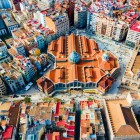Văzut de sus, Mercado de Colón se evidențiază în inima cartierului Eixample din Valencia: structura modernistă din cărămidă se integrează în rețeaua urbană densă și printre acoperișurile colorate.
