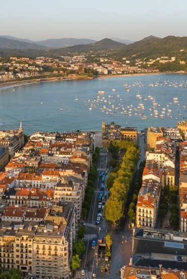 Văzut de sus, San Sebastián se deschide spre golful La Concha, printre bulevarde elegante, clădiri ordonate, plaje aurii și ambarcațiuni pe Marea Cantabrică.