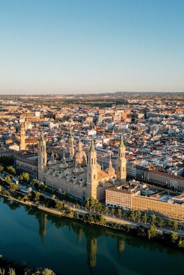 Vedere aeriană asupra Zaragozei de-a lungul râului Ebro: Basilica del Pilar domină centrul istoric prin turnurile și cupolele sale, simbol monumental și spiritual al orașului aragonez.
