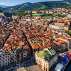 Văzut de sus, centrul vechi din Bilbao dezvăluie străzi înguste, acoperișuri roșii și clădiri istorice de-a lungul estuarului, cu Mercado de la Ribera în inima sa veche.