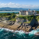 Palatul La Magdalena domină stâncile din Santander, printre roci modelate de mare, păduri de pini și apele cantabrice, având în fundal coasta muntoasă.