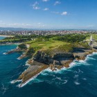 Vedere aeriană asupra Cabo Mayor, unde farul domină stâncile sculptate de Marea Cantabrică, între pajiști verzi și golfuri, cu Santander în fundal.