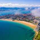 Vedere aeriană asupra orașului Santander și a plajei El Sardinero, o întindere aurie scăldată de Marea Cantabrică, între cartiere de coastă, peninsule verzi și dealuri.