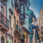 Calle Mon, vechea stradă a fierarilor, urcă printre fațade colorate, balcoane din fier și bovindouri asturiene, conducând privirea spre turnul gotic al Catedralei din Oviedo.
