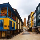 Calle Fierro străbate inima cartierului El Fontán printre fațade colorate, balcoane înflorite și galerii vitrate, conducând privirea spre turnul baroc al bisericii San Isidoro el Real.