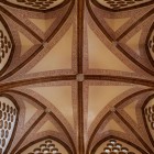 Privind în sus în Palatul Episcopal din Astorga, nervurile din cărămidă formează o cruce geometrică printre motive traforate: un detaliu în care Gaudí unește tehnica și imaginația.