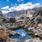 Printre stâncile vulcanice sculptate de ocean, un bazin natural reflectă cerul din Tenerife, iar impresionantele faleze Los Gigantes domină orizontul.