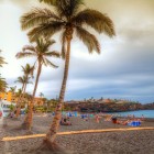 Pe Playa de La Arena, în Puerto de Santiago, palmierii și umbrelele însoțesc plaja cu nisip vulcanic negru, deschisă spre Atlantic sub un cer spectaculos la apus.