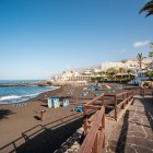 Promenada de la Playa de La Arena, în Puerto de Santiago, urmează caracteristica plajă cu nisip negru, printre palmieri, terase panoramice și albastrul Atlanticului.