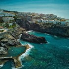 Văzută de sus, piscina naturală Isla Cangrejo se deschide printre rocile vulcanice din Puerto de Santiago, înconjurată de apele turcoaz ale Atlanticului și de casele cu vedere spre coastă.