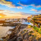 La apus, promenada din Puerto de Santiago urmează coasta vulcanică printre palmieri, terase și piscine cu vedere la Atlantic, în timp ce cerul se aprinde în nuanțe calde, aurii.