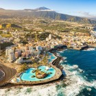 Vedere aeriană asupra orașului Puerto de la Cruz, cu complexul balnear Lago Martiánez, proiectat de César Manrique, coasta vulcanică și vulcanul Teide în fundal.