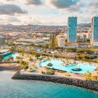 Parcul Maritim César Manrique se deschide spre ocean cu piscine cu apă sărată, palmieri și terase pentru plajă, în timp ce Turnurile din Santa Cruz conturează silueta modernă a capitalei insulei Tenerife.