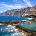 În Puerto de Santiago, o piscină naturală, încadrată de coasta vulcanică, oferă ape limpezi, iar în fundal se înalță stâncile Los Gigantes.