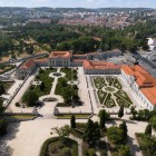 Vederea aeriană a Palatului Național Queluz dezvăluie armonia elegantă dintre aripile sale rococo și grădinile în stil francez, conturate de garduri vii geometrice, fântâni și alei spectaculoase.