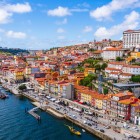 Vederea aeriană urmărește fluviul Douro de-a lungul animatului cartier Ribeira din Porto, unde fațadele colorate, terasele și vechile chei se desfășoară la poalele colinei, evocând sufletul comercial al orașului.
