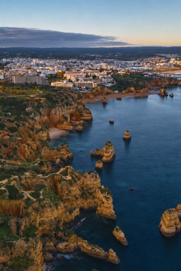 Vedere aeriană asupra orașului Lagos, unde falezele aurii din Ponta da Piedade coboară în Atlantic printre stânci izolate, golfuri ascunse și coasta luminoasă a regiunii Algarve.