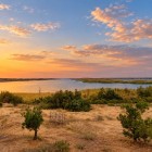 La apus, Lacul Aydarkul reflectă nuanțele aurii ale cerului, în timp ce vegetația deșertică încadrează un peisaj liniștit și surprinzător al Uzbekistanului.