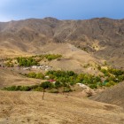 În fața călătorului, Munții Nuratau încadrează un mic sat: casele și grădinile verzi urmează cursul apei, dezvăluind viața rurală simplă dintre aceste văi aride.