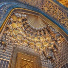Intrând în Madrasa Sher-Dor, privirea urcă spre elaboratele muqarnas, unde motivele geometrice, inscripțiile și detaliile aurii dezvăluie bogăția interiorului.