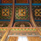 Privirea urcă spre un tavan ornamentat din lemn, alcătuit din vitralii colorate, sculpturi și motive geometrice policrome, care reflectă atenția acordată fiecărui detaliu.