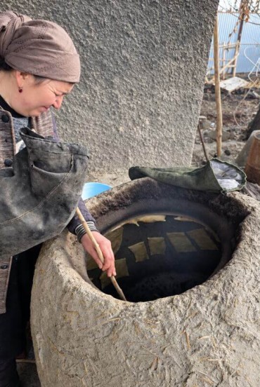 Gazda pregătește prânzul într-un kazan mare, așezat într-o vatră de pământ, prezentând o tehnică tradițională păstrată și folosită încă în bucătăria familiilor locale din sat.